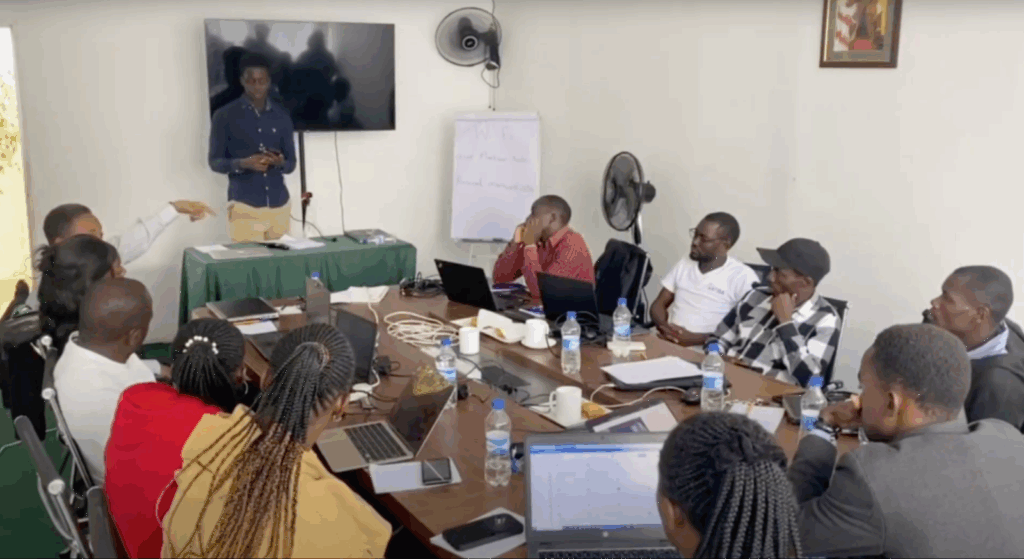 A facilitator stands at the front of the room as participants in the TeacherMatic Kenyan pilot engage in a group discussion, with laptops and notes on the table.
